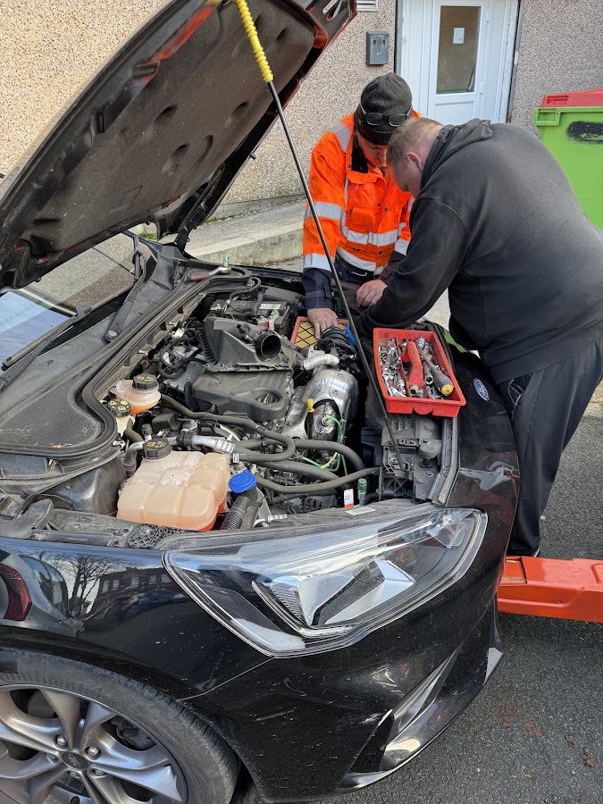 A Breakdown Man technician doing a roadside jump start under the bonnet.