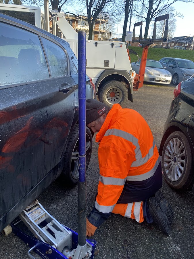 Simon changing a tyre in a car park.